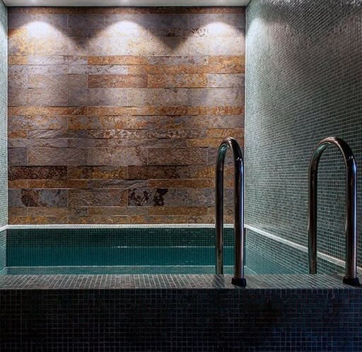 Bagnoturco_11 Piscina coperta con pareti in pietra e scala in acciaio, ambiente relax e wellness.