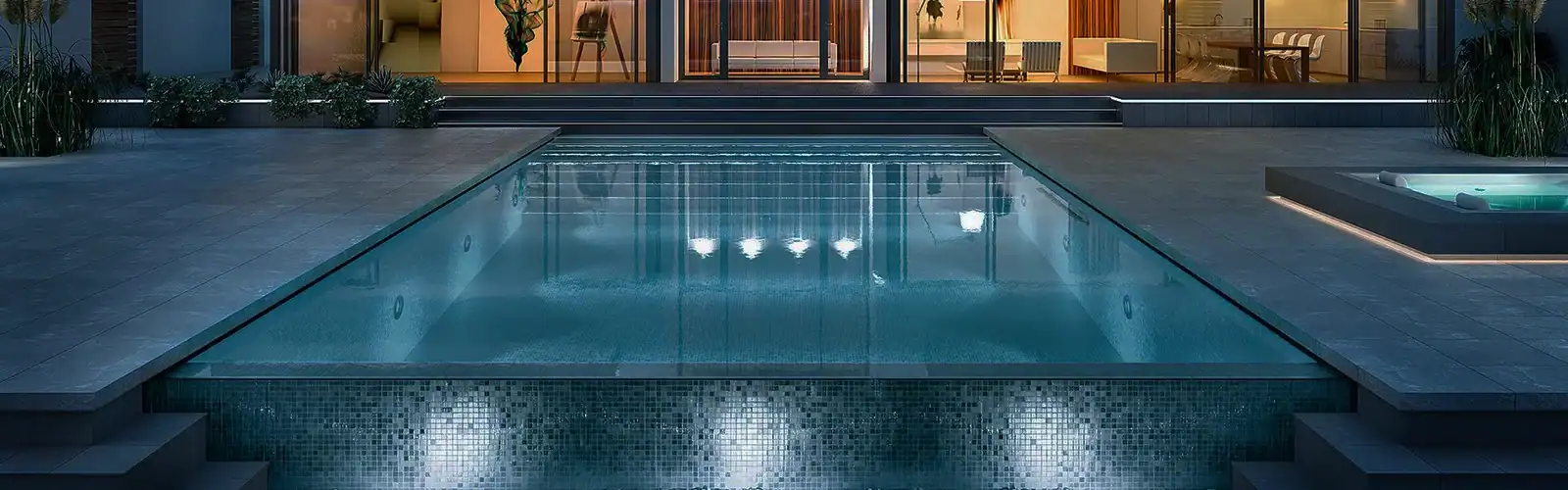 Piscina moderna a sfioro con illuminazione subacquea, di fronte a una casa elegante con vetrate.