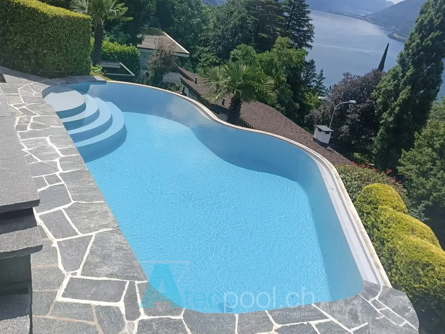 Piscina a forma libera con finitura in pietra e vista lago – Atec Pool Piscina a forma libera con scala circolare e vista panoramica sul lago