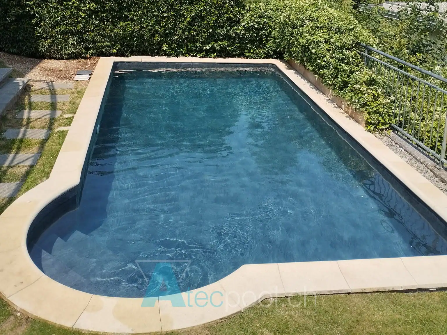 Piscina interrata con finitura scura e bordo in pietra – Atec Pool Piscina interrata con rivestimento blu e bordo in pietra naturale in un giardino