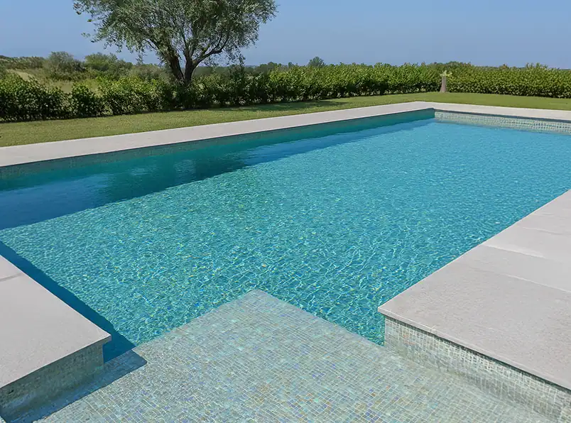 Piscina con rivestimento in mosaico elegante e luminoso Piscina moderna con rivestimento in mosaico azzurro e bordo in pietra chiara