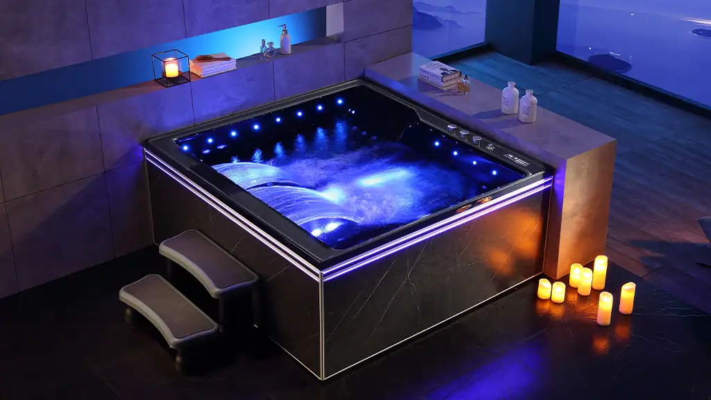 Whirlpool AT-6212 Minipiscina idromassaggio da interno con LED Relaxing hot tub with blue LED lighting, modern black exterior, and small steps in a spa room with candles and amenities, ideal for wellness and relaxation.