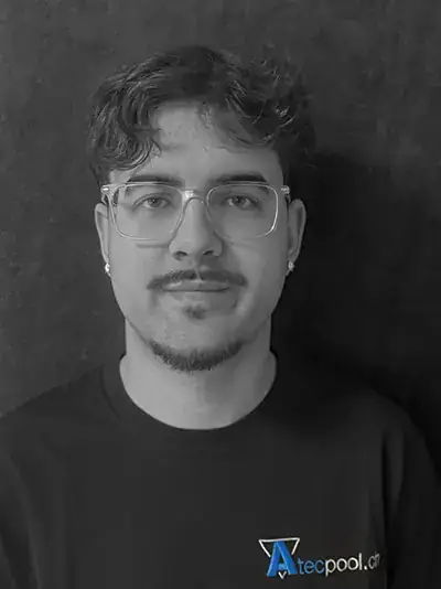 Ritratto di un uomo con occhiali, barba e capelli mossi, sfondo scuro.