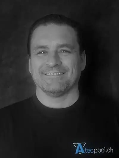 Ritratto di un uomo sorridente con sfondo scuro, abbigliamento casual, in ambiente professionale.