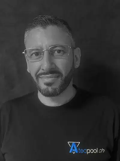 Uomo con barba e occhiali, sfondo scuro, abbigliamento nero con logo Atec Pool, primo piano, ritratto professionale.