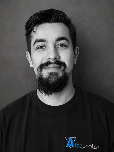 Ritratto di un uomo con barba e capelli scuri, maglietta nera con logo Atec Pool, sfondo grigio.